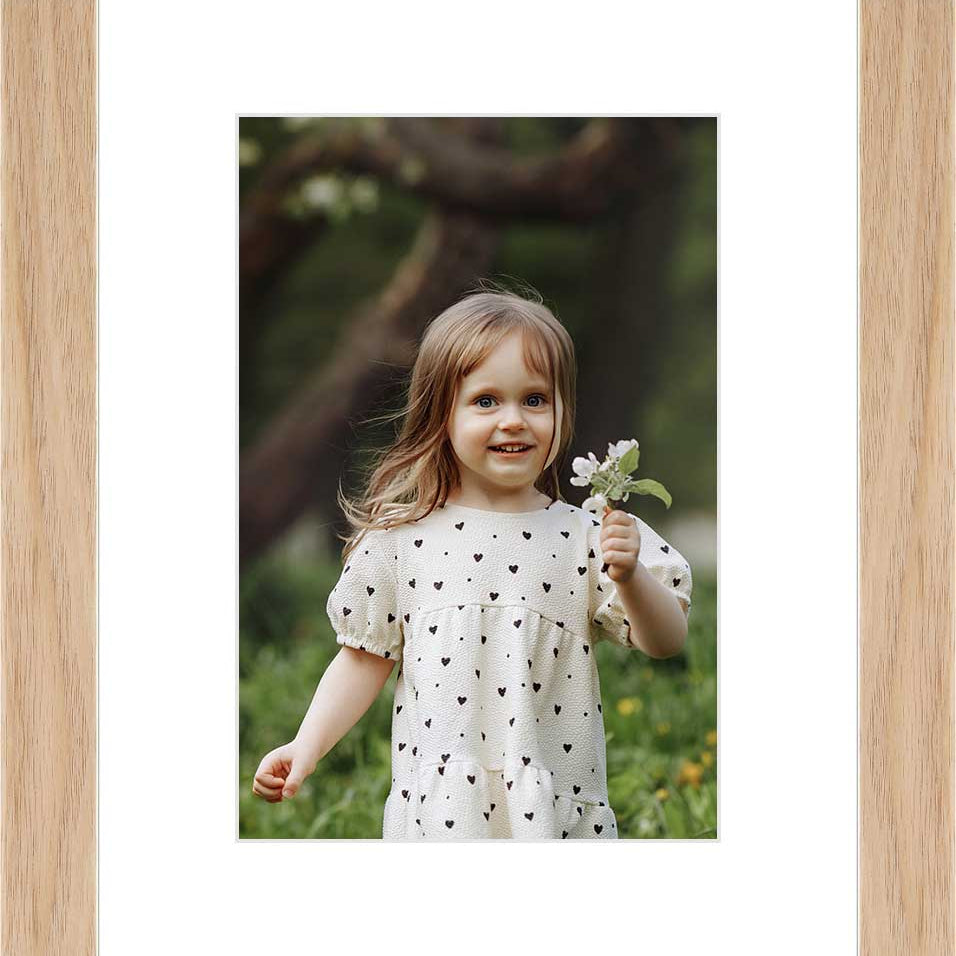 "Framed photo of a young girl holding a flower in an outdoor setting. "