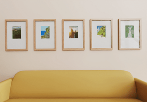 Five framed pictures on a wall above a yellow sofa