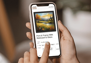 Person holding a smartphone displaying an art print ordering app with a scenic image on screen.